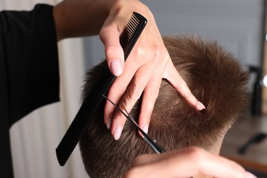 Photo of Professional hairdresser cutting client's hair with scissors in barbershop, closeup