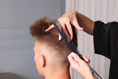 Photo of Professional barber making stylish haircut in salon, closeup