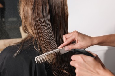 Hairdresser using spray while making stylish haircut in salon, closeup