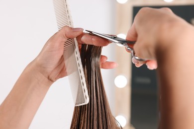 Hairdresser cutting client's hair with scissors in salon, closeup