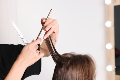 Photo of Hairdresser cutting client's hair with scissors in salon, closeup