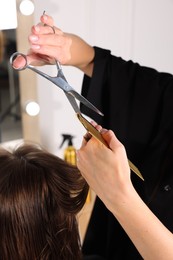 Photo of Hairdresser cutting client's hair with scissors in salon, closeup