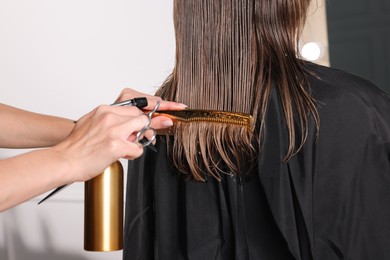 Hairdresser using spray while making stylish haircut in salon, closeup