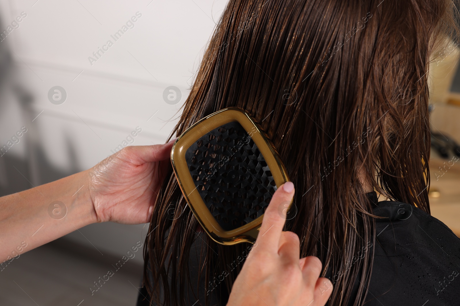 Photo of Hairdresser brushing client's wet hair in salon, closeup