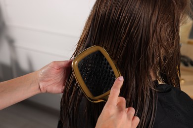 Hairdresser brushing client's wet hair in salon, closeup