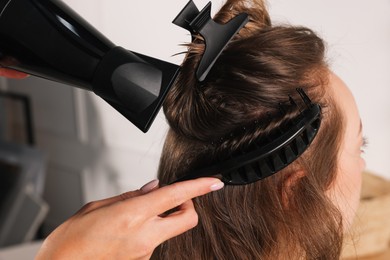 Hairdresser blow drying client's hair in salon, closeup