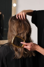 Hairdresser brushing client's hair in salon, closeup