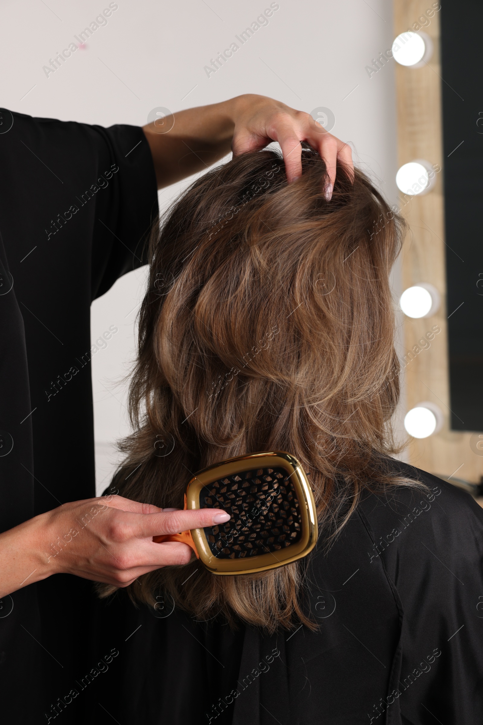 Photo of Hairdresser brushing client's hair in salon, closeup