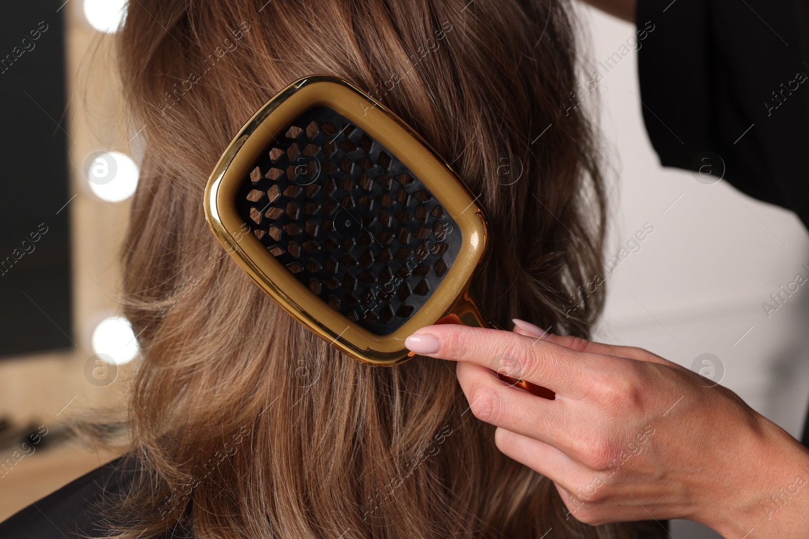 Photo of Hairdresser brushing client's hair in salon, closeup