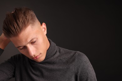 Photo of Confident young man with stylish haircut on black background. Space for text