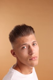 Confident young man with stylish haircut on light brown background