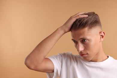 Confident young man with stylish haircut on light brown background. Space for text