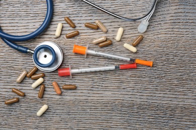 Pharmacist. Many different pills, stethoscope and syringes on wooden table, flat lay