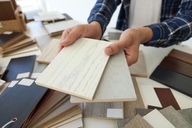 Photo of Man choosing wooden flooring among different samples at table, closeup