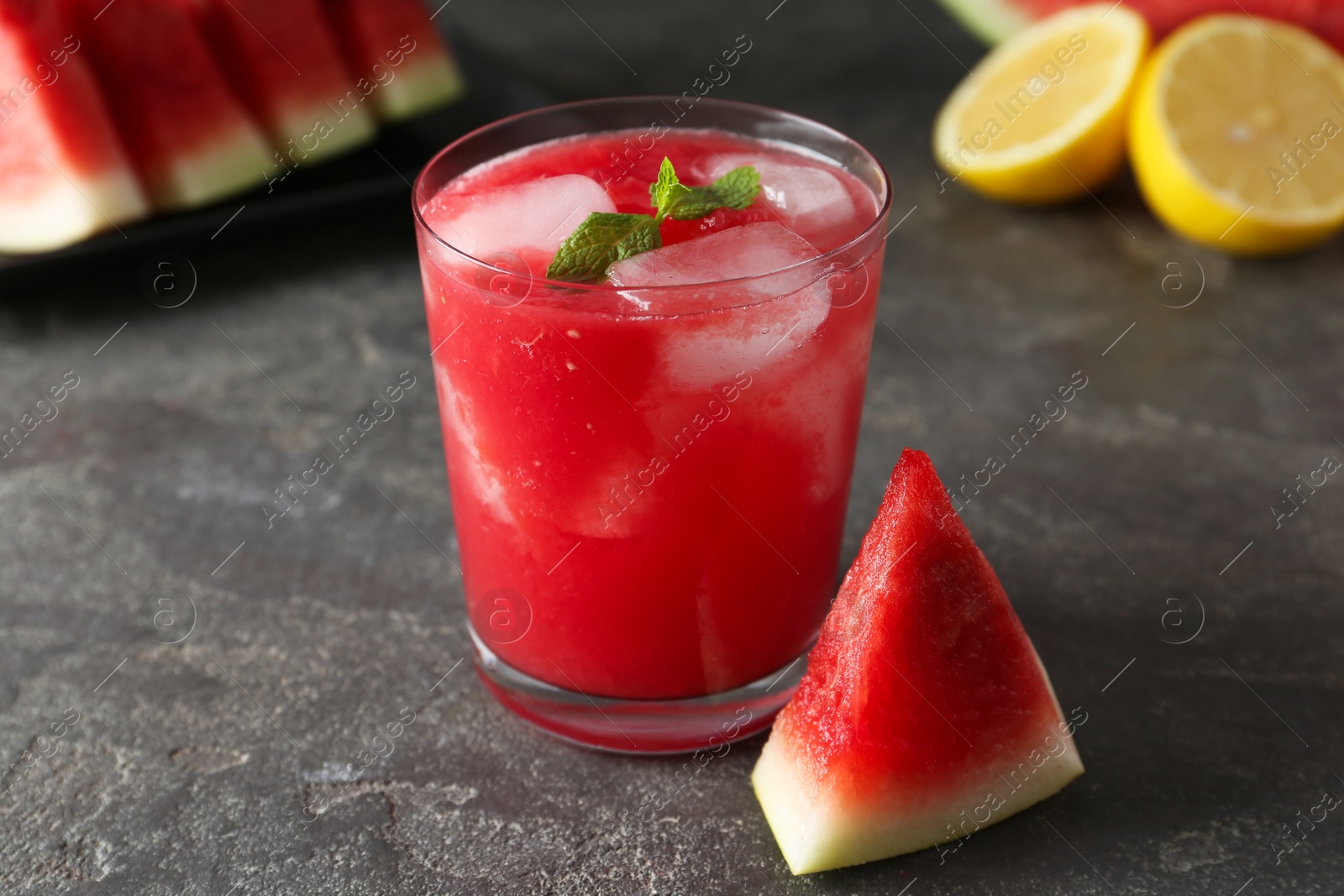 Photo of Tasty watermelon drink in glass, fresh fruits and mint on grey table, closeup