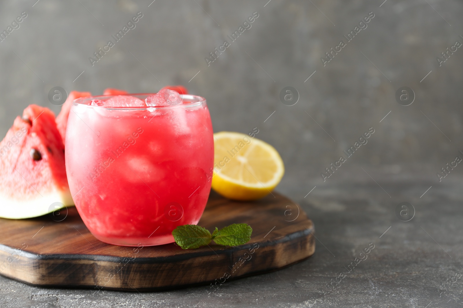 Photo of Tasty watermelon drink in glass, fresh fruits and mint on grey table, closeup. Space for text