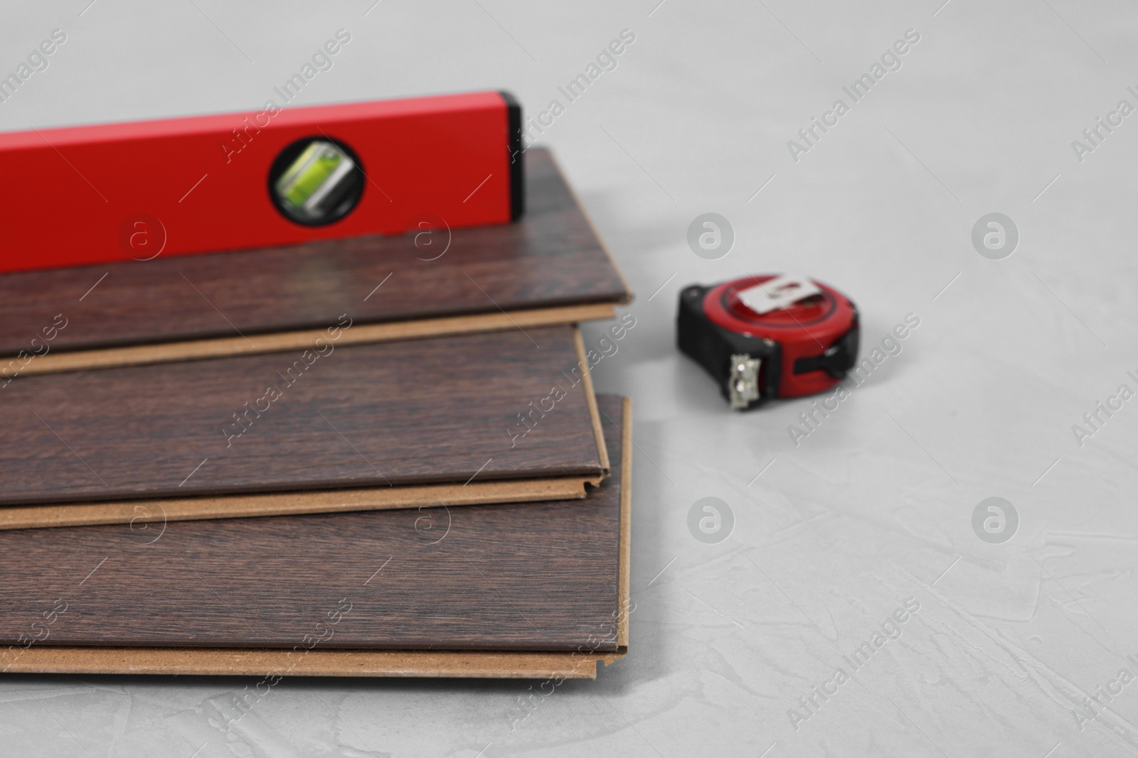 Photo of Measuring tape, level tool and laminate flooring pieces on grey textured surface, closeup