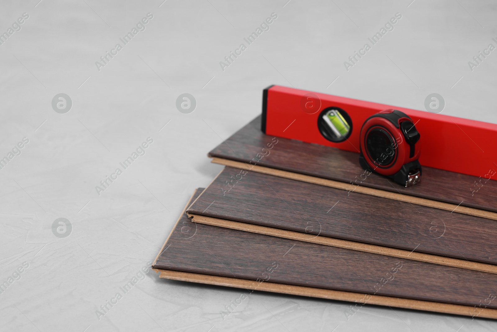 Photo of Measuring tape, level tool and laminate flooring pieces on grey textured surface, closeup