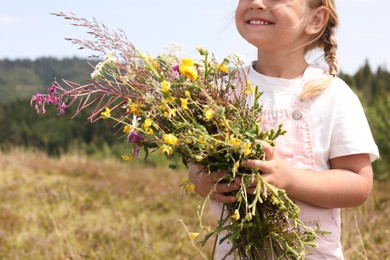 Photo of Smiling little girl with bouquet of wildflowers at field, closeup