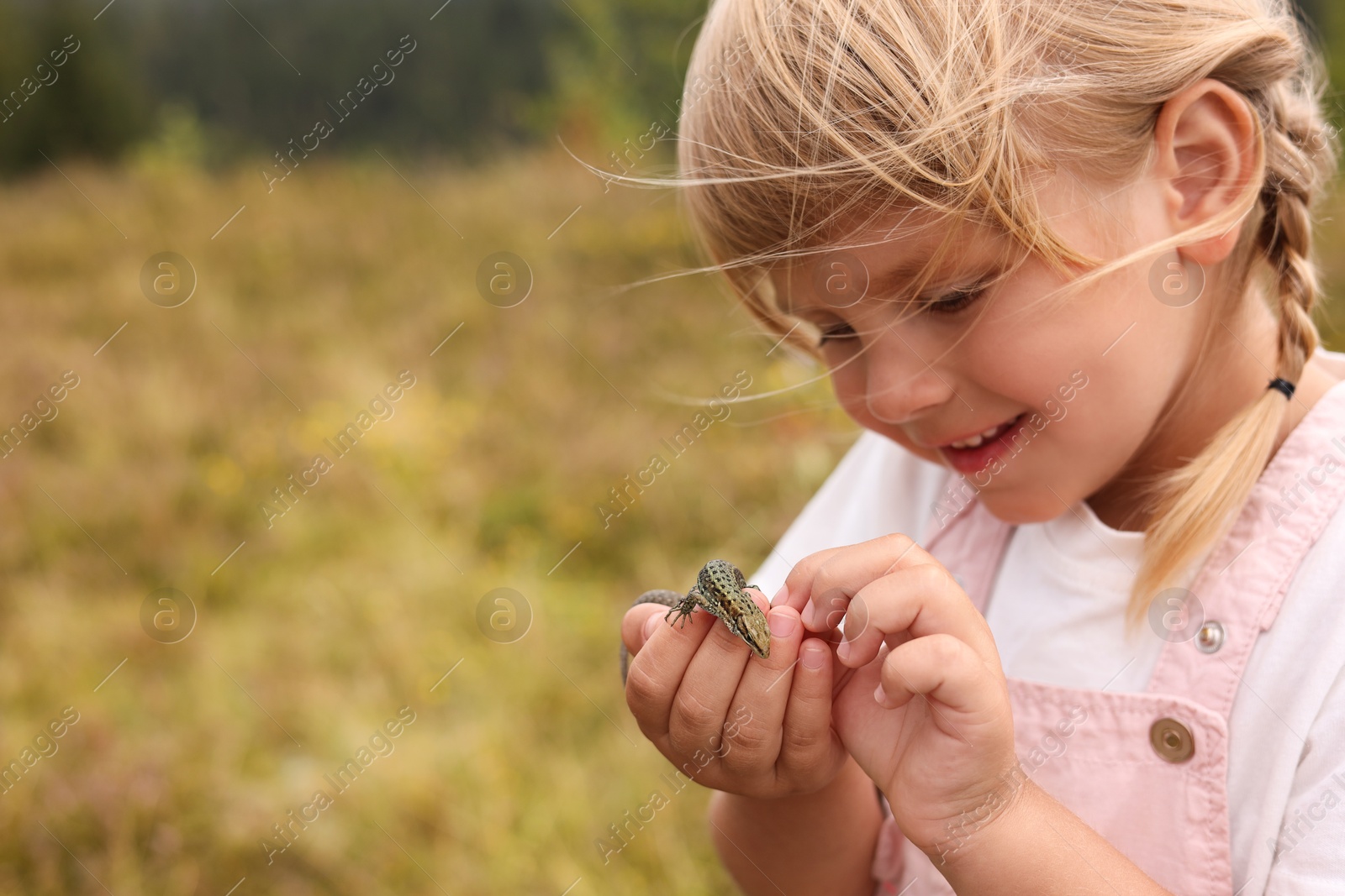 Photo of Happy little girl holding small lizard outdoors, space for text