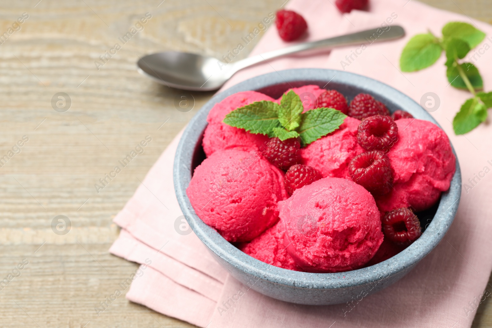 Photo of Delicious raspberry sorbet with fresh berries in bowl and spoon on wooden table, closeup