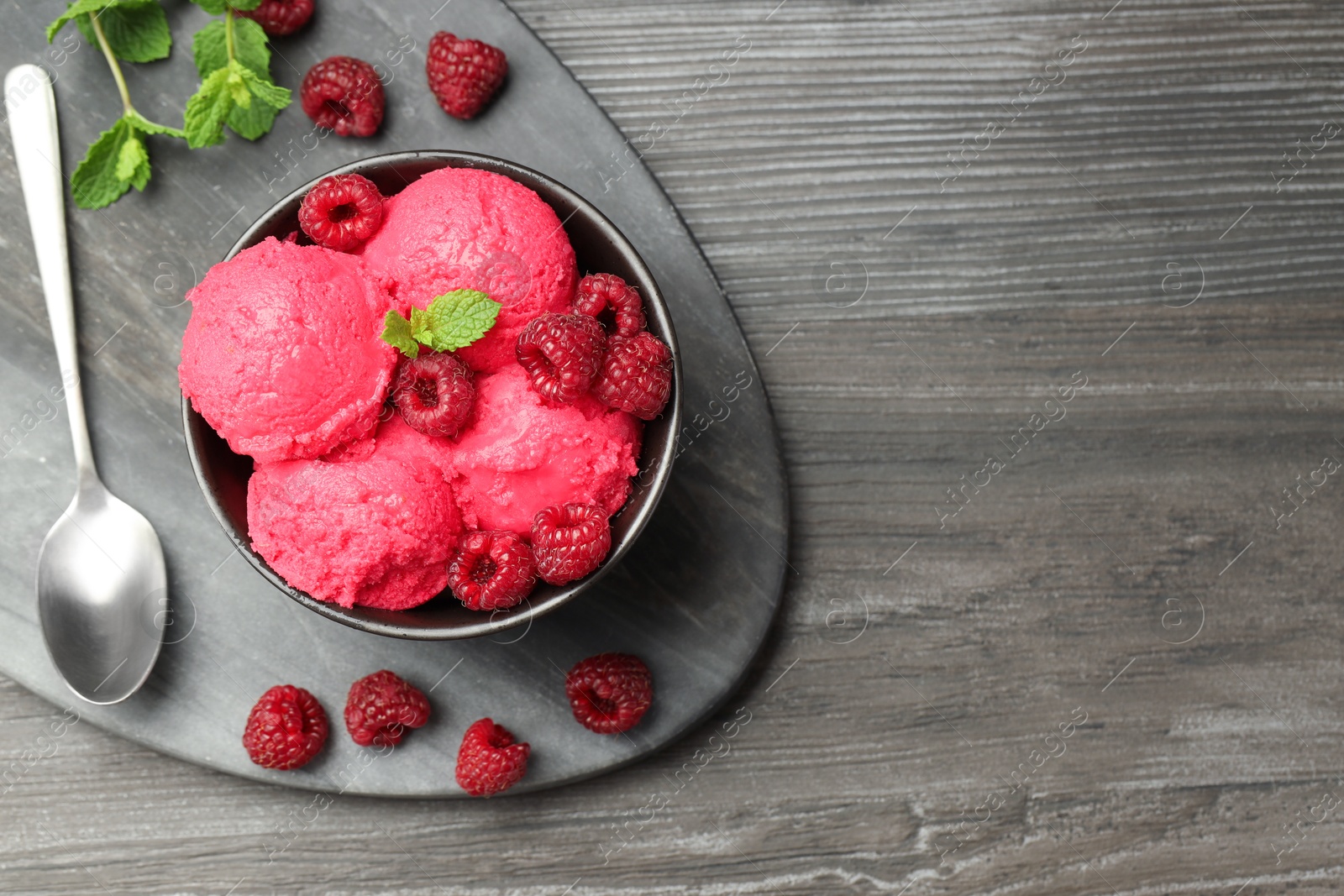 Photo of Delicious raspberry sorbet in bowl, fresh berries, mint and spoon on wooden table, top view. Space for text