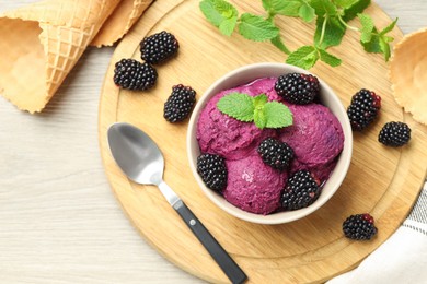 Delicious blackberry sorbet with fresh berries in bowl, waffle cones and spoon on wooden table, flat lay