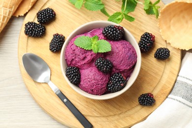 Photo of Delicious blackberry sorbet with fresh berries in bowl, waffle cones and spoon on wooden table, top view