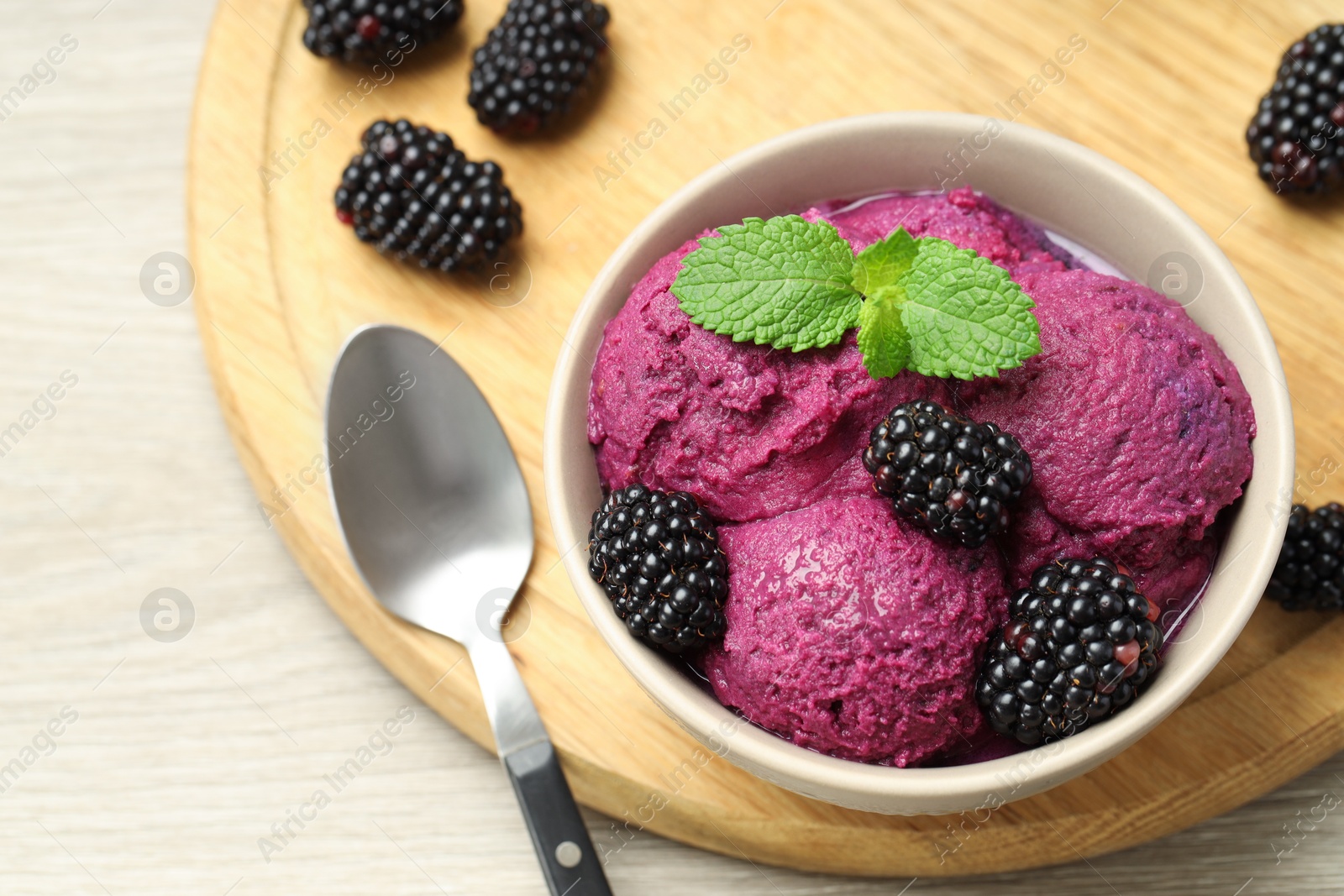 Photo of Delicious blackberry sorbet with fresh berries in bowl and spoon on wooden table, above view