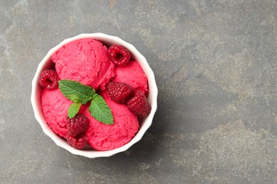 Photo of Delicious raspberry sorbet, fresh berries and mint in bowl on gray textured table, top view. Space for text