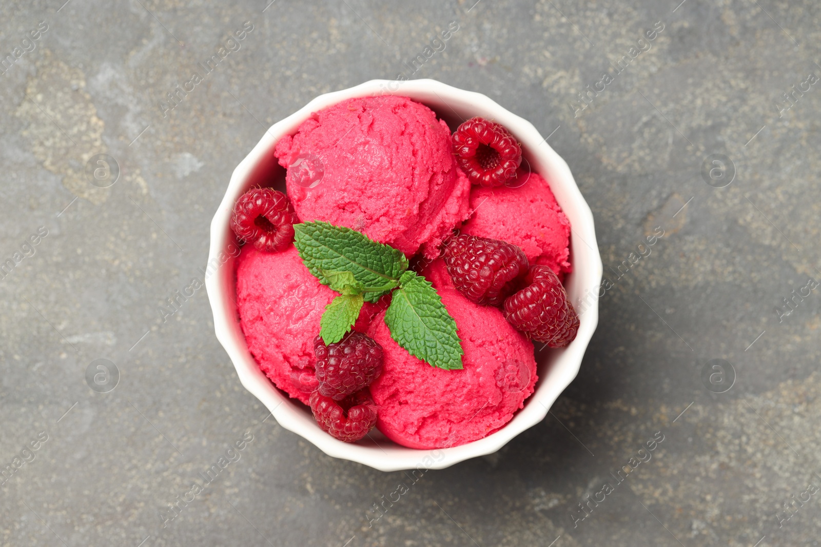 Photo of Delicious raspberry sorbet, fresh berries and mint in bowl on gray textured table, top view