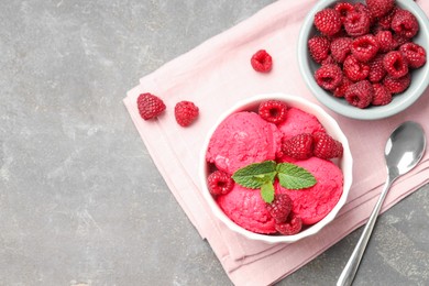 Photo of Delicious raspberry sorbet with fresh berries in bowl and spoon on gray textured table, flat lay. Space for text