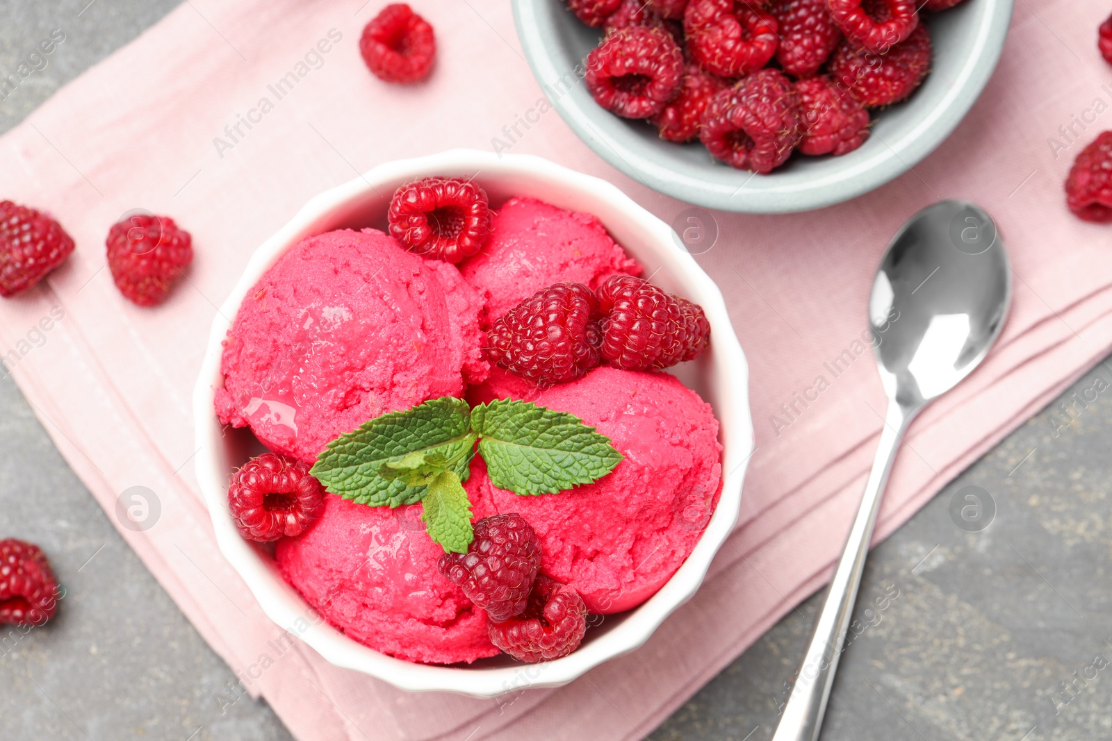 Photo of Delicious raspberry sorbet with fresh berries in bowl and spoon on gray textured table, flat lay