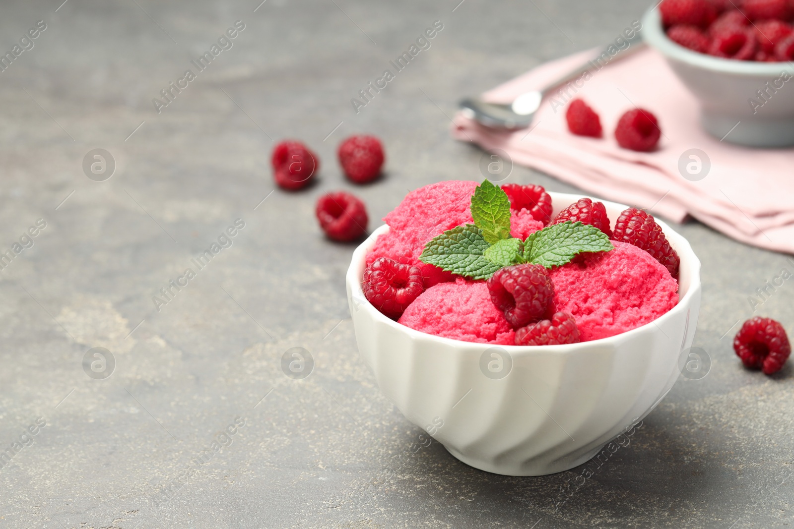 Photo of Delicious raspberry sorbet, fresh berries and mint in bowl on gray textured table, space for text