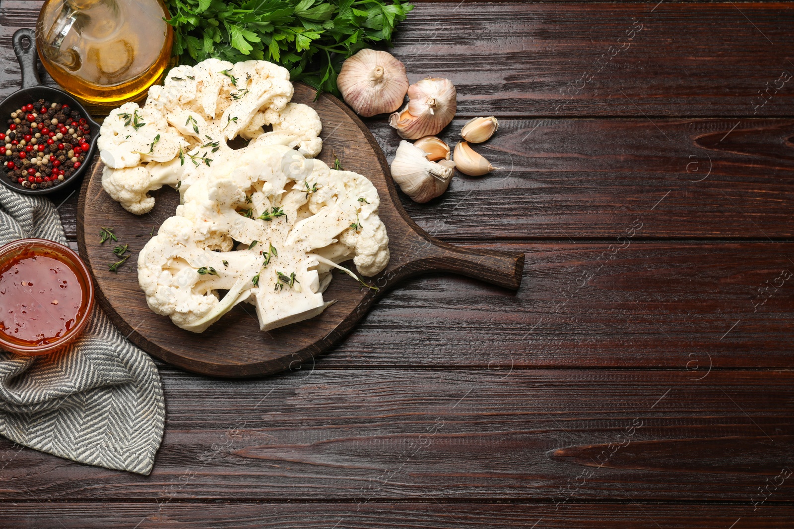 Photo of Uncooked cauliflower steaks, sauce, oil and spices on wooden table, flat lay. Space for text