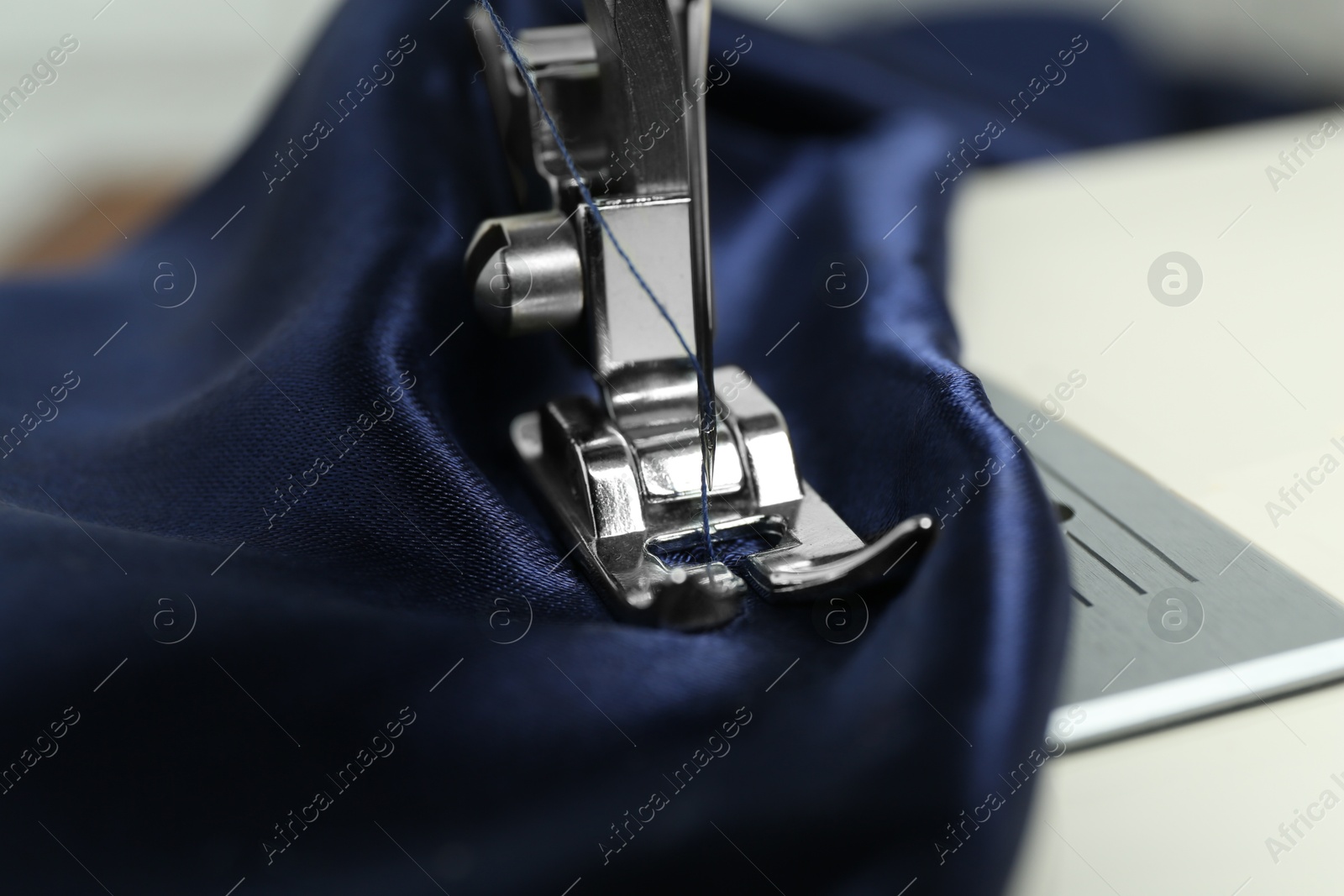 Photo of Sewing machine with blue fabric, closeup view