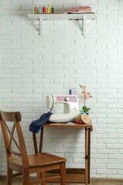 Sewing machine, blue fabric and craft accessories on wooden table near white brick wall