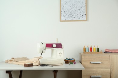 Sewing machine, beige fabric and craft accessories on light table indoors