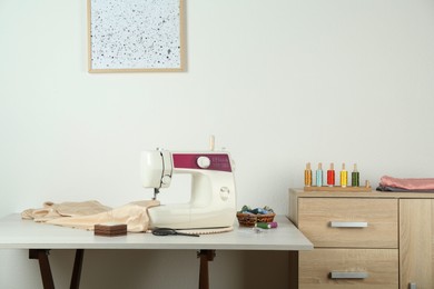 Sewing machine, beige fabric and craft accessories on light table indoors