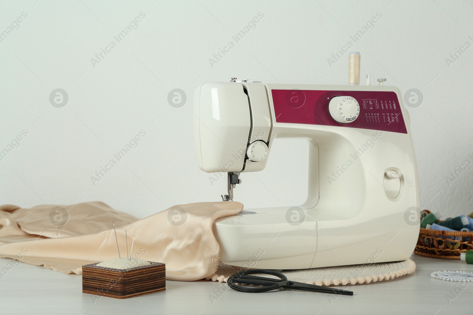 Photo of Sewing machine, beige fabric and craft accessories on wooden table indoors