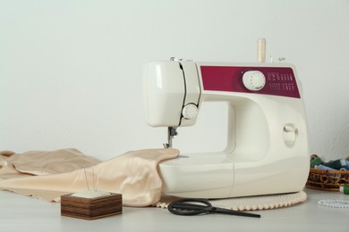 Photo of Sewing machine, beige fabric and craft accessories on wooden table indoors