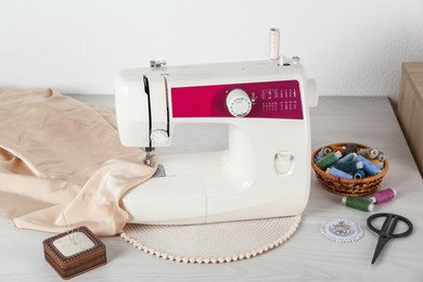 Photo of Sewing machine, beige fabric and craft accessories on wooden table indoors