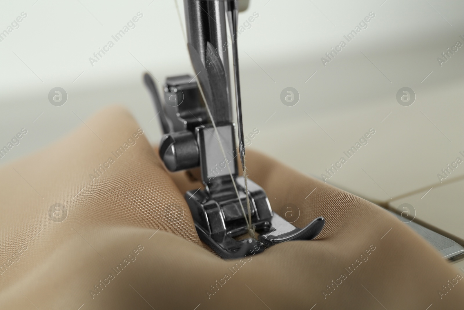 Photo of Sewing machine with beige fabric on light background, closeup