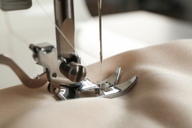 Photo of Sewing machine with beige fabric on light background, closeup