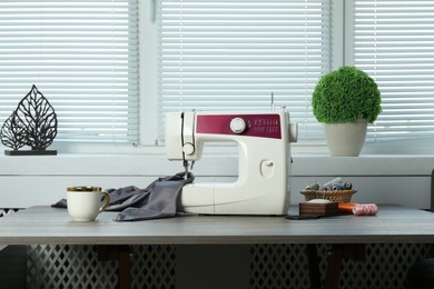 Photo of Sewing machine, gray fabric and craft accessories on wooden table indoors