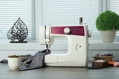 Photo of Sewing machine, gray fabric and craft accessories on wooden table indoors