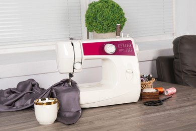 Sewing machine, gray fabric and craft accessories on wooden table indoors