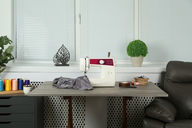 Photo of Sewing machine, gray fabric and craft accessories on wooden table indoors