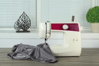 Photo of Sewing machine with gray fabric on wooden table indoors