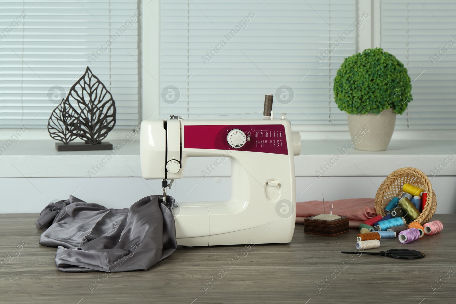 Photo of Sewing machine, gray fabric and craft accessories on wooden table indoors